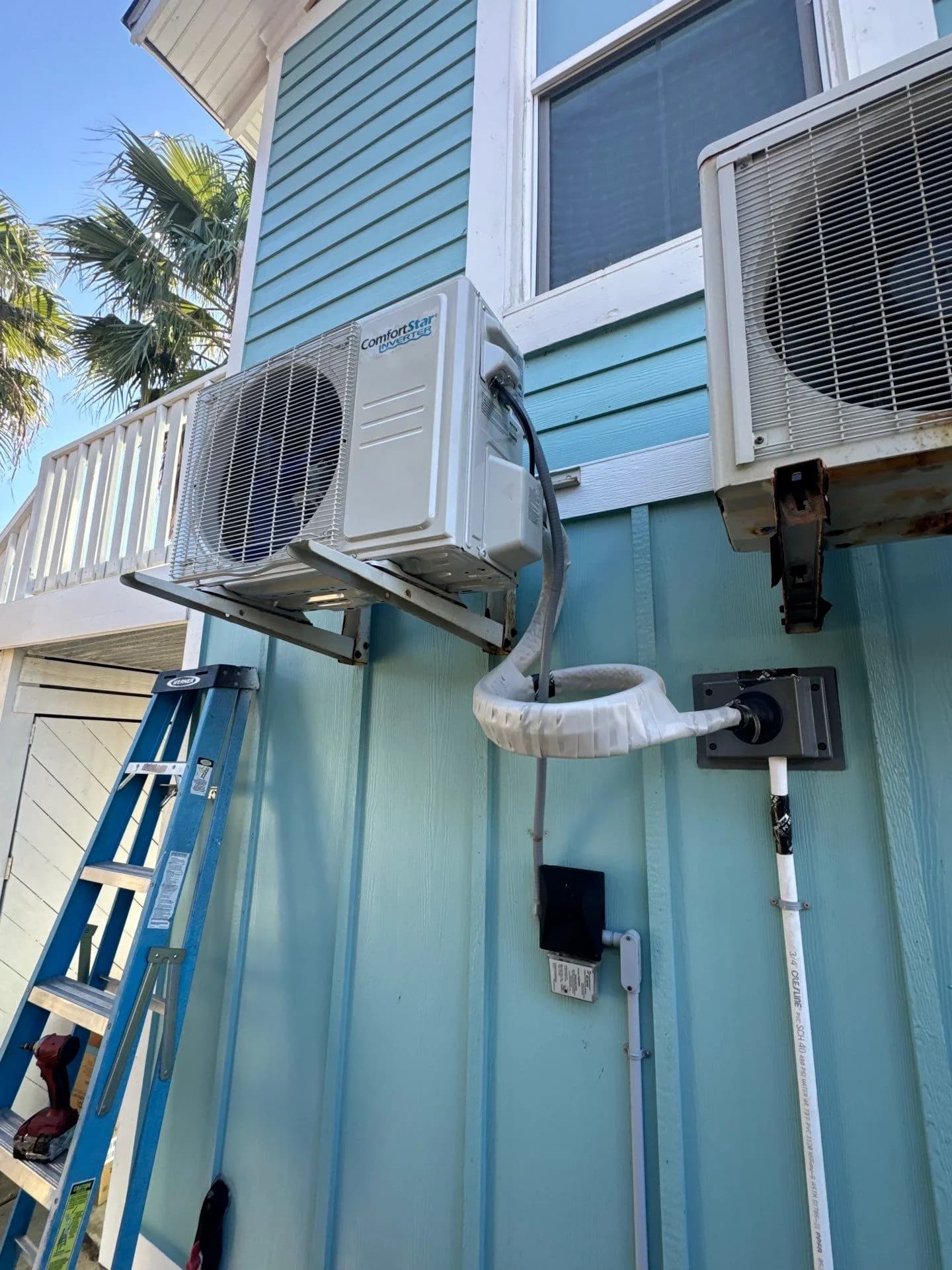 Ductless mini-split AC installation on a blue house exterior with palm trees nearby.